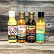 Four bottles of Barba Cuban sauce on a wooden surface with a textured gray background