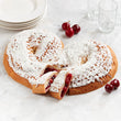 Heart-shaped kringle with white icing and red cherries on a marble surface