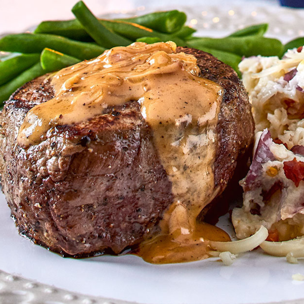 Tenderloin with Parmesan Cream sauce on a plate with cheesy potatoes and green beans. 