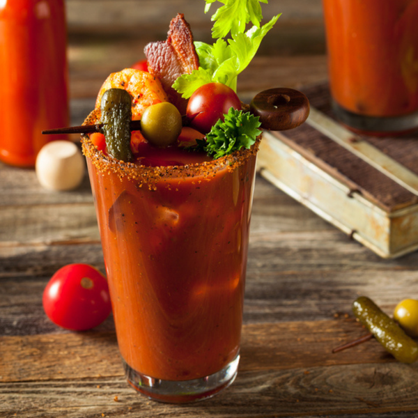 Bloody Mary on wooden table with cornichon,olives, shrimp, bacon, tomatoes and celery
