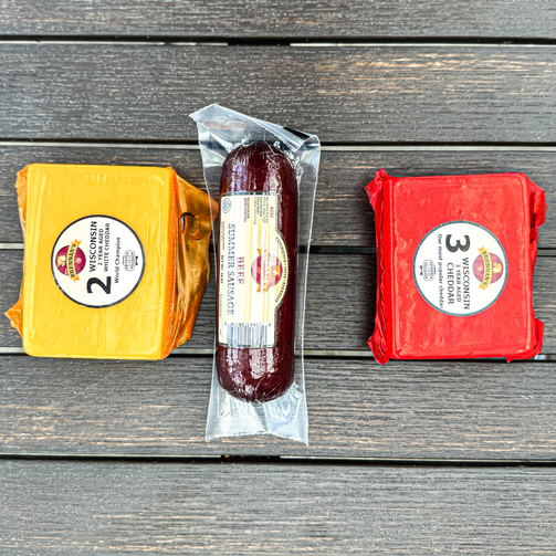 Three packages of cheese and a sausage on a wooden surface