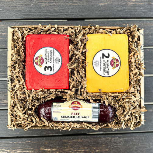 Gift set with two blocks of cheese and a package of summer sausage in a decorative box on a wooden surface.