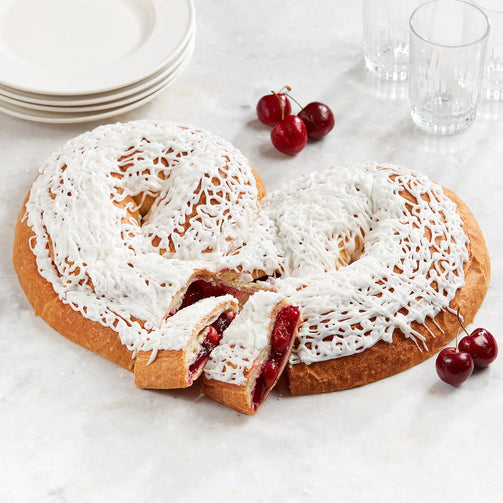 Heart-shaped kringle with white icing and red cherries on a marble surface